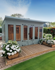 Welford summer house with double doors and large windows on a wooden deck in a landscaped garden by IN Sheds